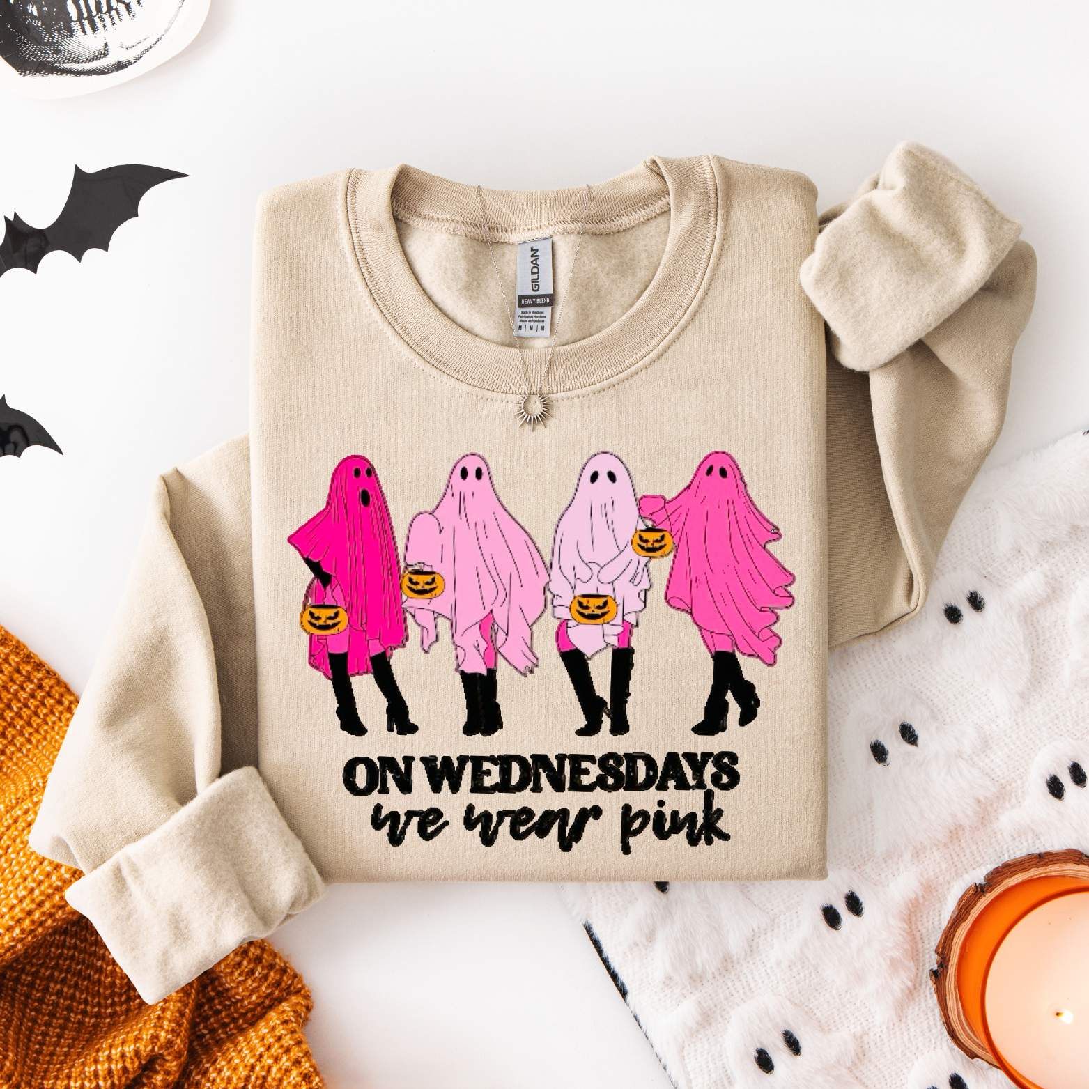 Beige sweatshirt with pink ghosts and text on a white surface with Halloween decorations.