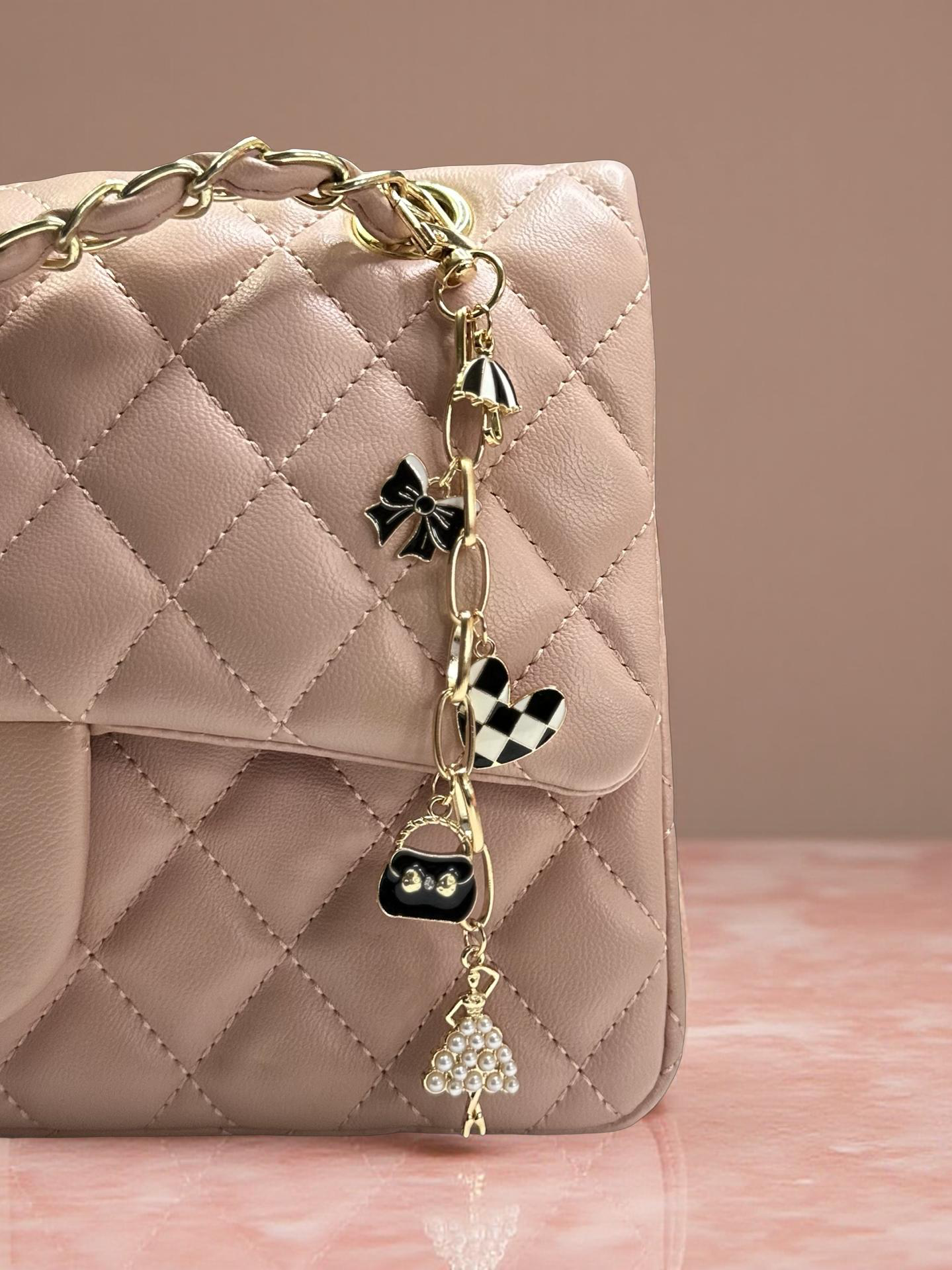 Quilted pink handbag with decorative charm on a pink surface