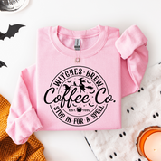 Pink sweatshirt with 'Witches Brew Coffee Co.' text on a Halloween-themed background